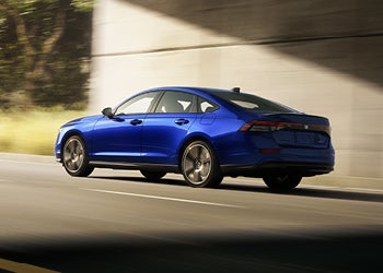 Blue sedan driving on a road beside a modern concrete wall, captured in motion.