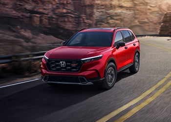 Red Honda SUV driving on a winding road with rocky cliffs in the background.
